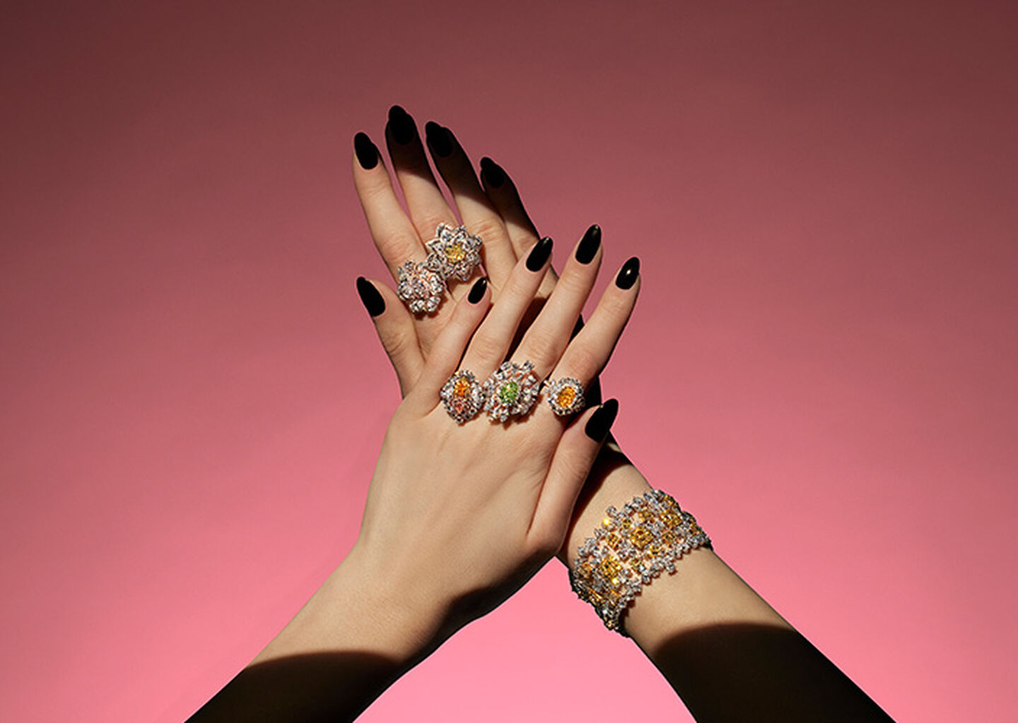 A woman's hand wearing coloured diamond high jewellery necklace by Maison Birks on a red background.